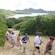 A group of adults in lightweight clothes walk up a winding trail through brush and trees overlooking a bay